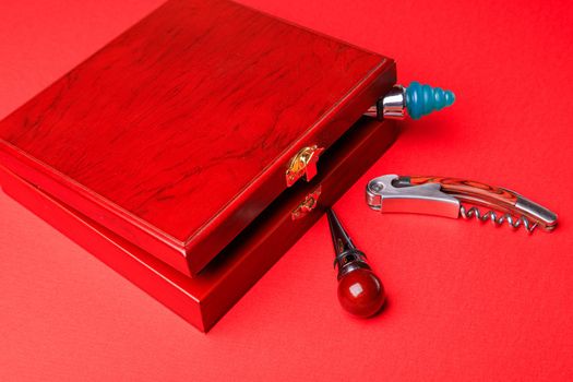 Gift set of corkscrew and removable lids. Wine corks and bottle openers in a wooden box on a red background.