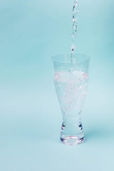 A jet of water fills transparent glass against a blue background. White bubbles rise.