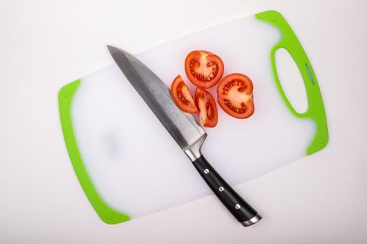 On a cutting board is a fresh red cut tomato and a large chef's knife. On an isolated white background.