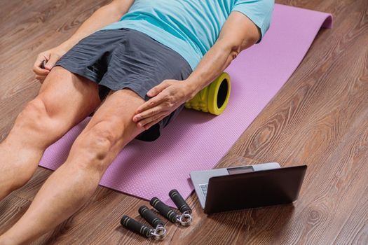 50-year-old man performs exercises while lying on the rug at home, looking at the computer. During a pandemic, a person trains in an apartment via the Internet.