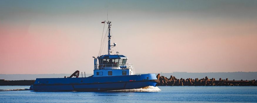 Blue small tug ship sailing past the breakwater dam in morning