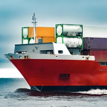 Red cargo container ship's bow in cloudy day