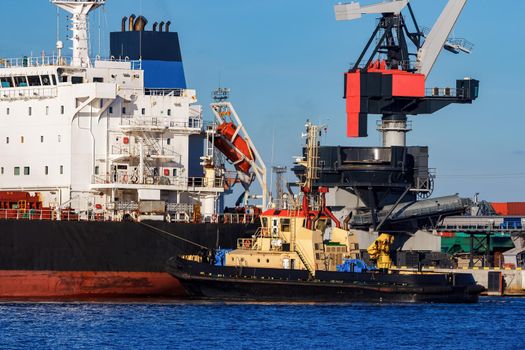 Black cargo ship mooring at the port with tug ship support