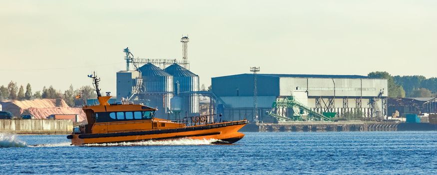Orange pilot ship sailing past the factory in Latvia