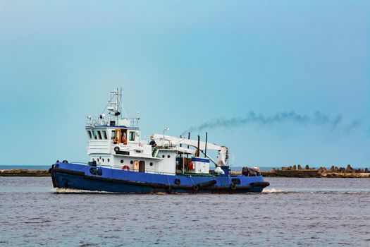 Blue tug ship moving to the cargo terminal. Industrial services