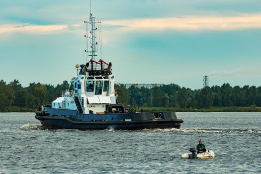 Black tug ship moving to the cargo terminal. Industrial service