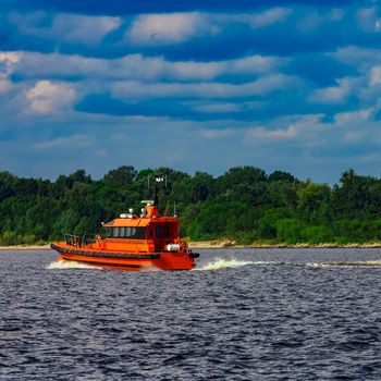 Orange pilot boat moving by the river in Europe. Rescue service