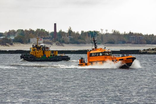 Orange pilot ship moving at speed past the tug ship in Riga