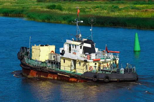 Old tug ship moving to the cargo terminal. Industrial service