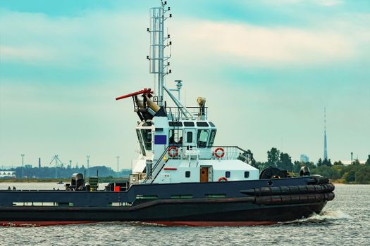 Black tug ship moving to the cargo terminal. Industrial service