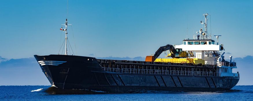 Black Sailing Bulk Carrier. Cargo Ship with Long Reach Excavator Moving in Still Water at Sunny Day by the Sea