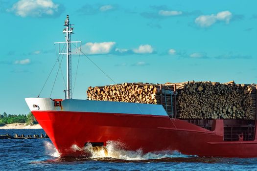 Red cargo ship fully loaded with wood moving at clear day