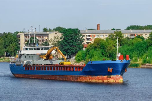 Blue cargo ship with long reach excavator moving to the port