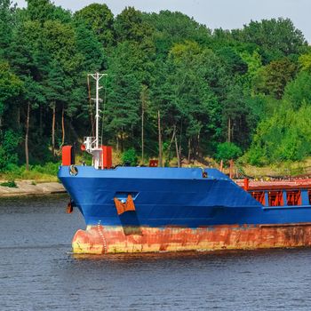 Blue cargo ship with long reach excavator moving to the port