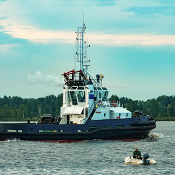 Black tug ship moving to the cargo terminal. Industrial service