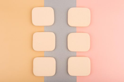 Minimalistic flat lay with with two rows of square shaped make up sponges against colored pink, silver and beige background. High quality photo