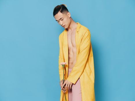 Sexy man with a naked torso in a yellow coat with a flower in his hand. High quality photo