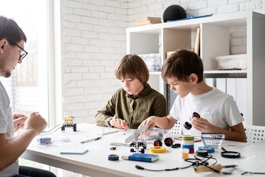 Young boys and teacher having fun constructing robot cars together at the workshop