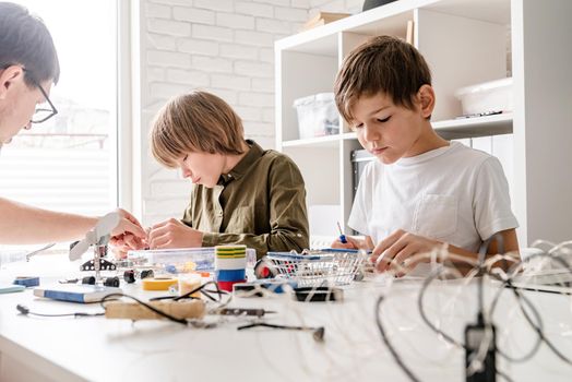 Young boys and teacher having fun constructing robot cars together at the workshop