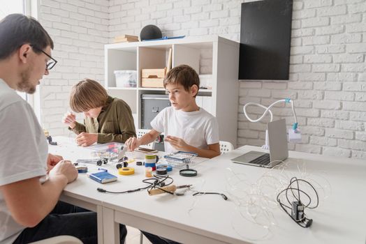 Young boys and teacher having fun constructing robot cars together at the workshop