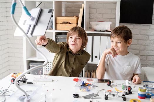 young boys having fun making robot cars watching education programme on digital tablet, pointing finger