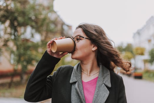 Attractive young woman drinking coffee from a paper cup and looking away