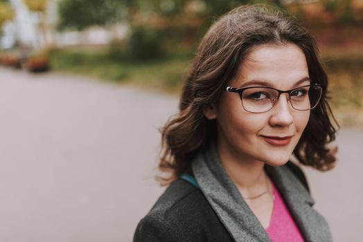 Portrait of a pretty young bespectacled female with red lips smiling cheerfully while being outdoors