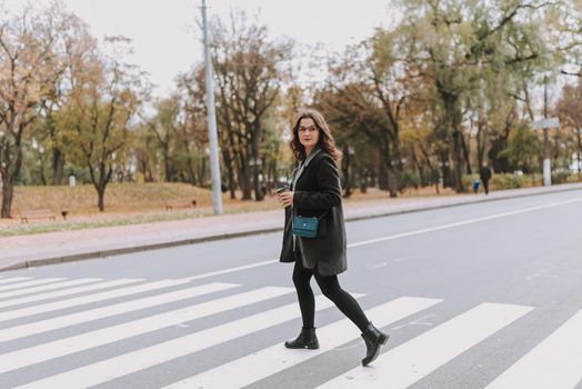 Beautiful young woman holding a paper cup of coffee and turning back while crossing the road on a crosswalk