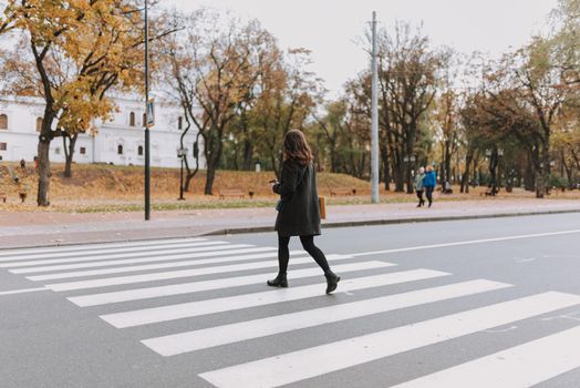 Woman with coffee following the rules and crossing the road on pedestrian crosswalk