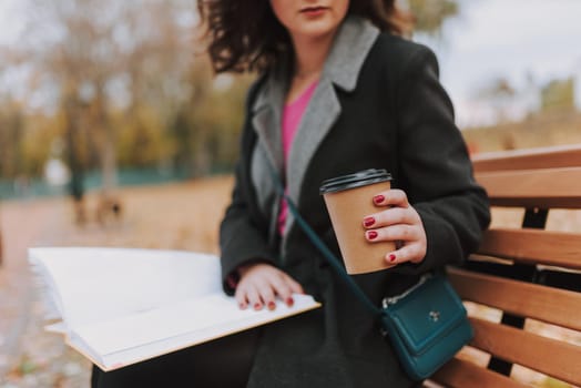 Cropped photo of female student with coffee sitting on the bench while studying with book outdoors
