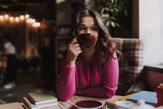 Beautiful lady wearing glasses and enjoying tea while having lunch and holding cup