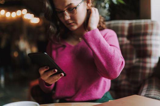 Cropped photo of pretty lady sitting in coffee house and typing on smartphone