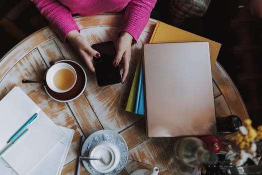 Top view of female hands holding mobile phone while sitting at the table in coffee house