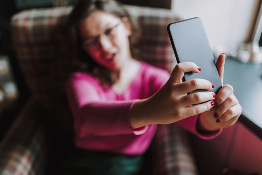 Smiling young lady posing on smartphone camera while taking selfie in cafe