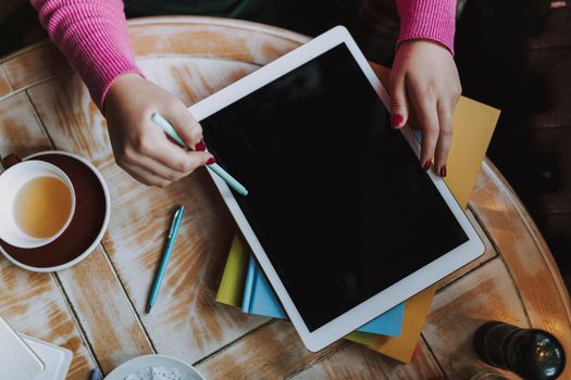 Top view of woman sitting at wooden table and using digital tablet and drinking tea