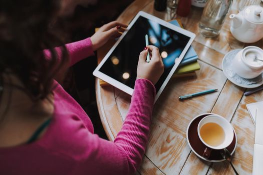 Top view of Caucasian woman using digital tablet while sitting at wooden table in cafe