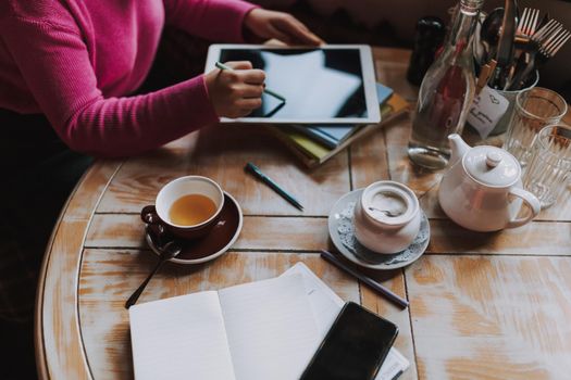 Top view of cup of tea on wooden table and lady using digital tablet in coffee house