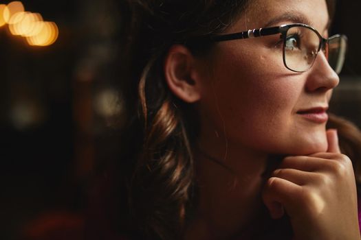 Close up of pretty woman wearing glasses and looking away while holding hand on chin