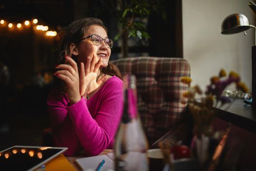 Happy beautiful sitting at the table in coffee house while waving to her friend outside the window