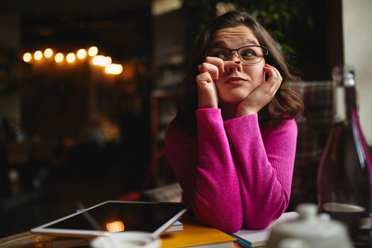 Funny pretty woman wearing glasses resting from job and making grimace in cozy cafe