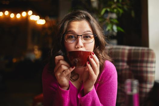 Waist up of beautiful lady wearing glasses while enjoying coffee in cozy cafe