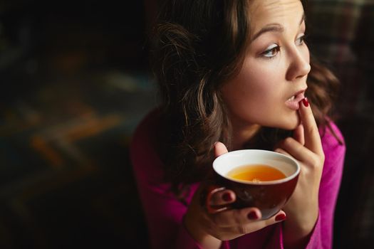 Close up of attractive lady touching lips and holding red cup of tea in coffee house
