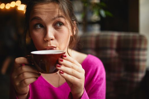 Attractive brunette enjoying hot drink while holding red cup in her hands in cafe