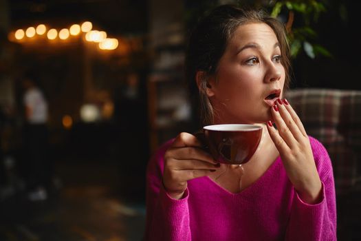 Waist up of pretty young brunette having break with coffee while holding red cup