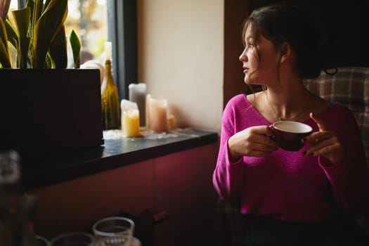 Beautiful brunette looking out the window while enjoying coffee in cozy coffee house