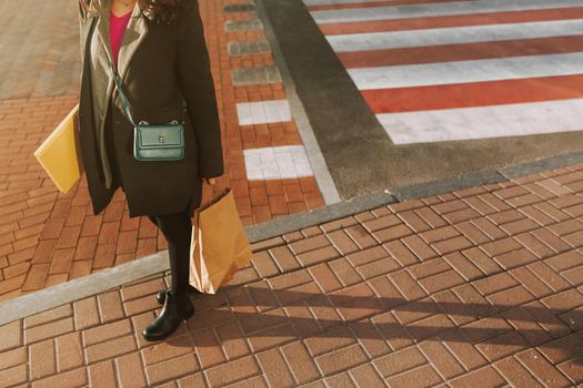 Cropped photo of lady in coat standing on sidewalk while holding shopping bag