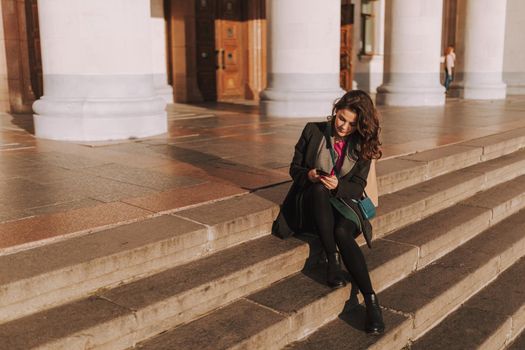 Smiling young woman typing on smartphone while sitting on steps during sunny day