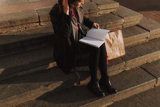 Beautiful lady resting on stairs while holding book and reading. Shopping bag next to woman