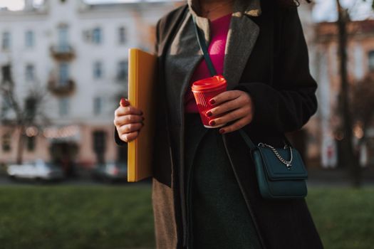 Cropped phot of lady posing on the street while holding coffee and folder