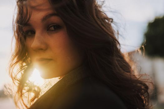 Close up of attractive brunette lady in black coat walking outdoors and looking at camera